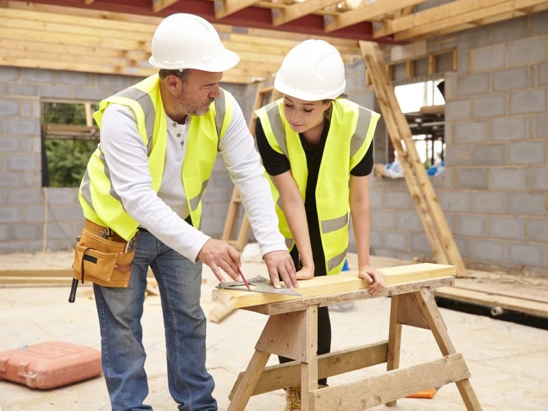 Carpenter With Female Apprentice Working On Building Site